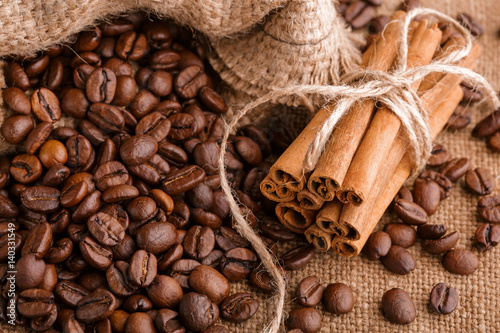 Coffee beans and cinnamon on a background of burlap. Roasted coffee beans background close up. Coffee beans pile from top with copy space for text. Seasoning. Spice. Cinnamon. Badian. Coffee house. © stas_malyarevsky