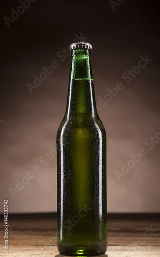 Glass bottle of beer on brown background