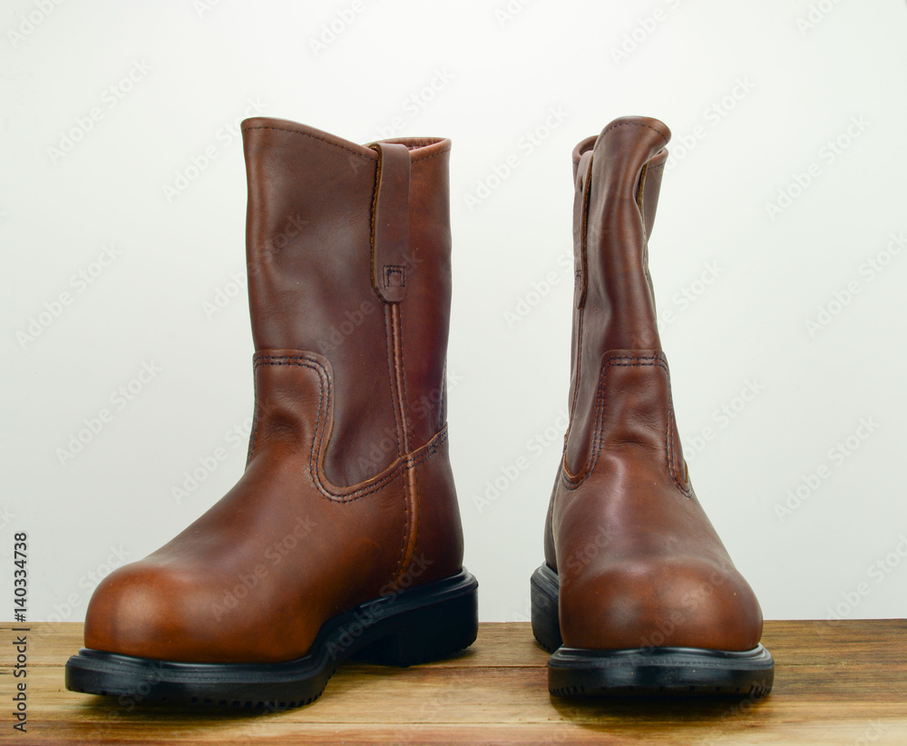 A pair of brown color leather safety boot with white background on a wooden surface A pair of brown color leather safety boot with white background on a wooden surface