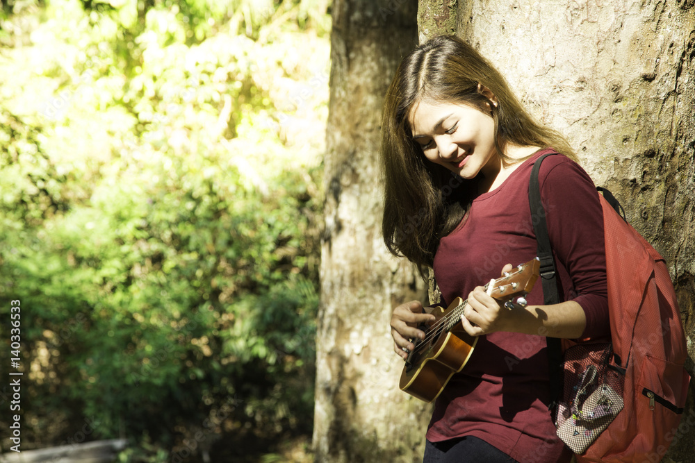Young Beautiful Asian Woman is sitting and playing guitar,Woman playing acoustic guitar in central park Cute young adult girl sit big forest. Young Beautiful Asian Woman is sitting and playing guitar,Woman playing acoustic guitar in central park Cute young adult girl sit big forest.