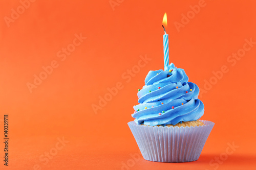 Tasty cupcake with candle on orange background