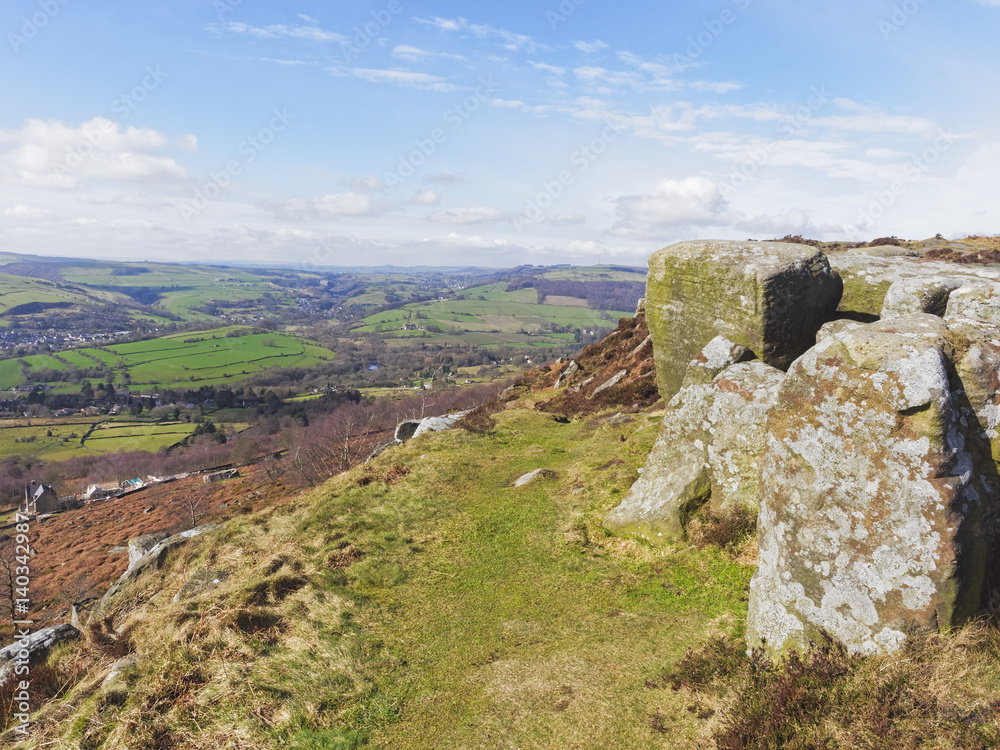 A narrow path overlooking the Derbyshire Dales runs between gritstone boulders and the edge of a steep hill