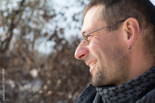 Close up portrait in profile of happy adult man with glasses and beard bristle outdoors