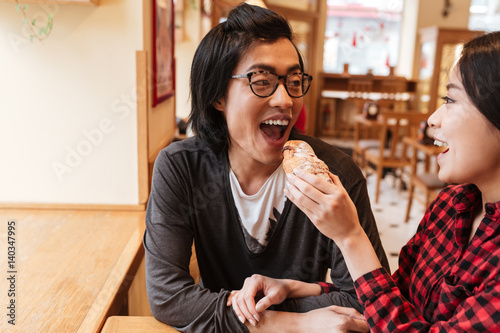 Happy asian young loving couple eating croissant.