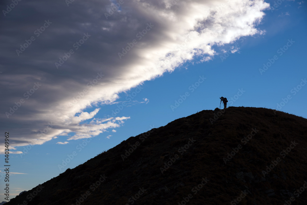 Silhouette of a photographer on a hill on the background of clouds (lifestyle, changes go - concept)
