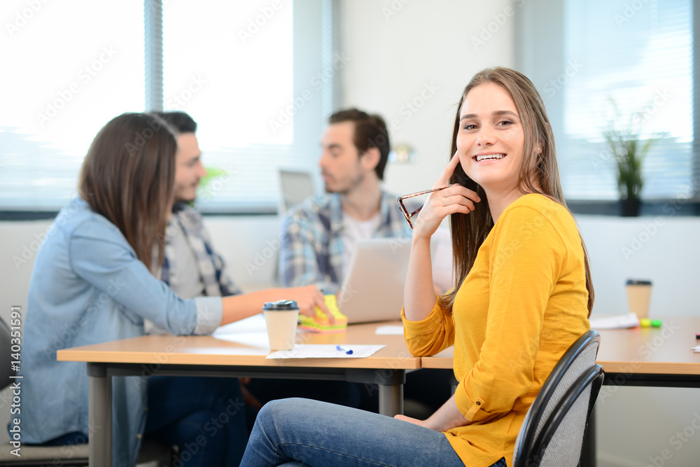 portrait of young woman in casual wear working in a creative business startup company office with coworker people in background portrait of young woman in casual wear working in a creative business startup company office with coworker people in background