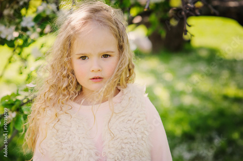 spring portrait of beautiful dreamy curly 5 years old child girl walking in blooming garden