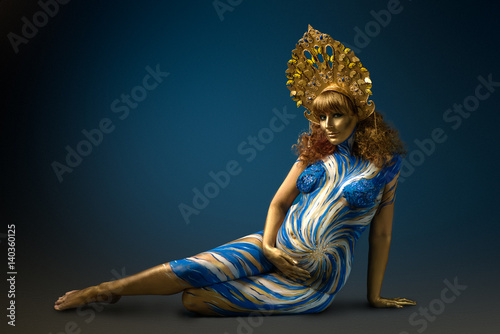 Fotografie Fashionable redhead pregnant woman with kokoshnik and abstract body art in shade