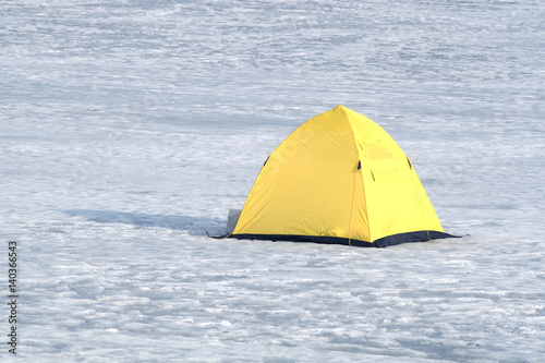 Fisherman tent from yellow with black bottom in snow on frozen river in winter day closeup