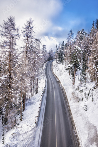 Asphalt curved road leading to high snowy mountains behind fog, winter season