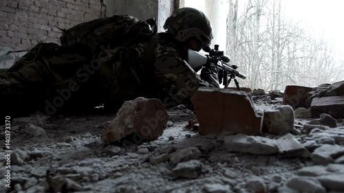 Military man with arms lies in ambush in an abandoned building