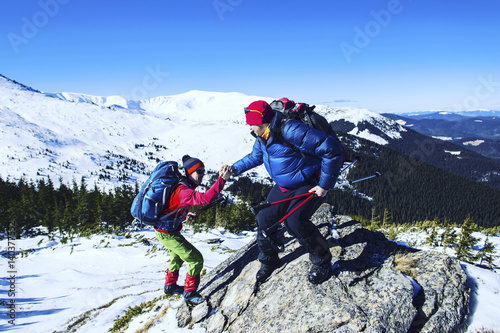 Man giving helping hand to friend to climb mountain rock cliff.