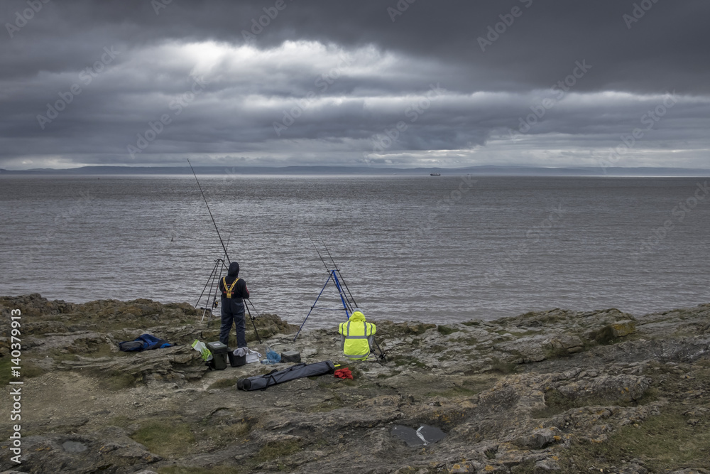 Two fishermen, on the shore in Barry, South Wales, on a stormy overcast day