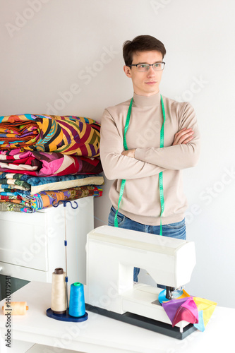 handsome young male tailor holding a stack of folded colors patchwork quilts on a white background. Many colorful blankets in style patchwork in the hands of the smiling man  handmade.