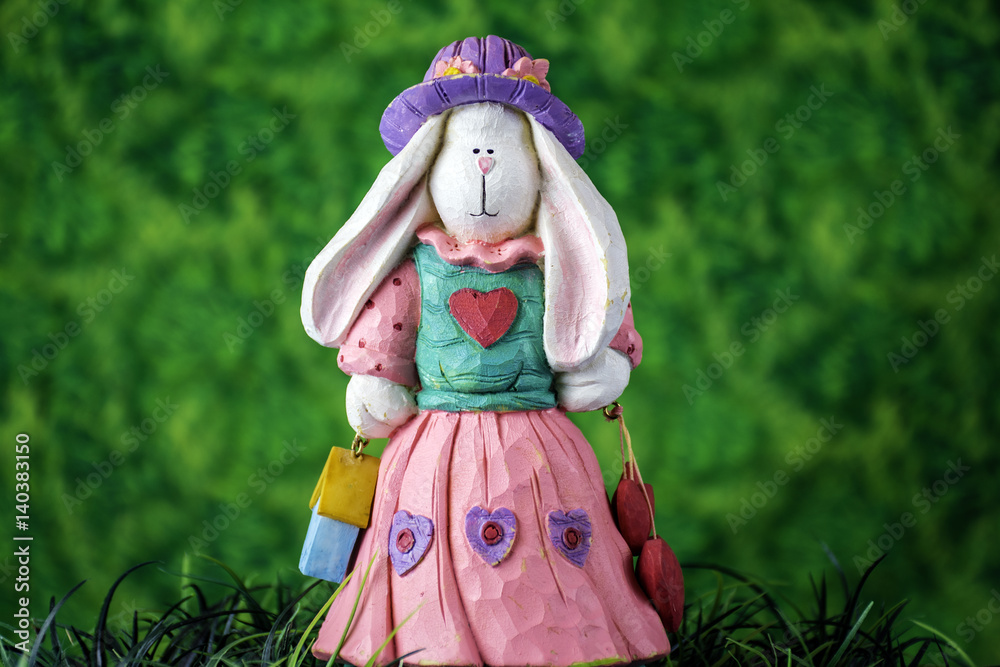 white female rabbit figurine wearing a purple hat and pink dress standing in green grass
