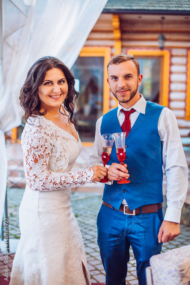 Young newlyweds clinking decorated glasses and enjoying romantic moment together at wedding reception outside