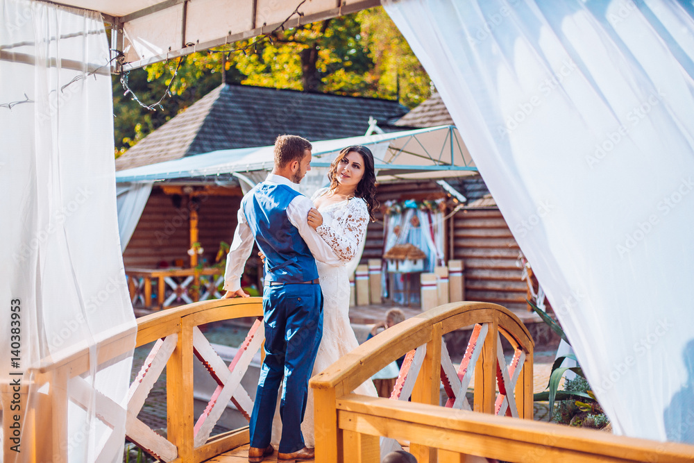 Handsome happy romantic groom and beautiful sensual bride in white dress posing under tent Handsome happy romantic groom and beautiful sensual bride in white dress posing under tent