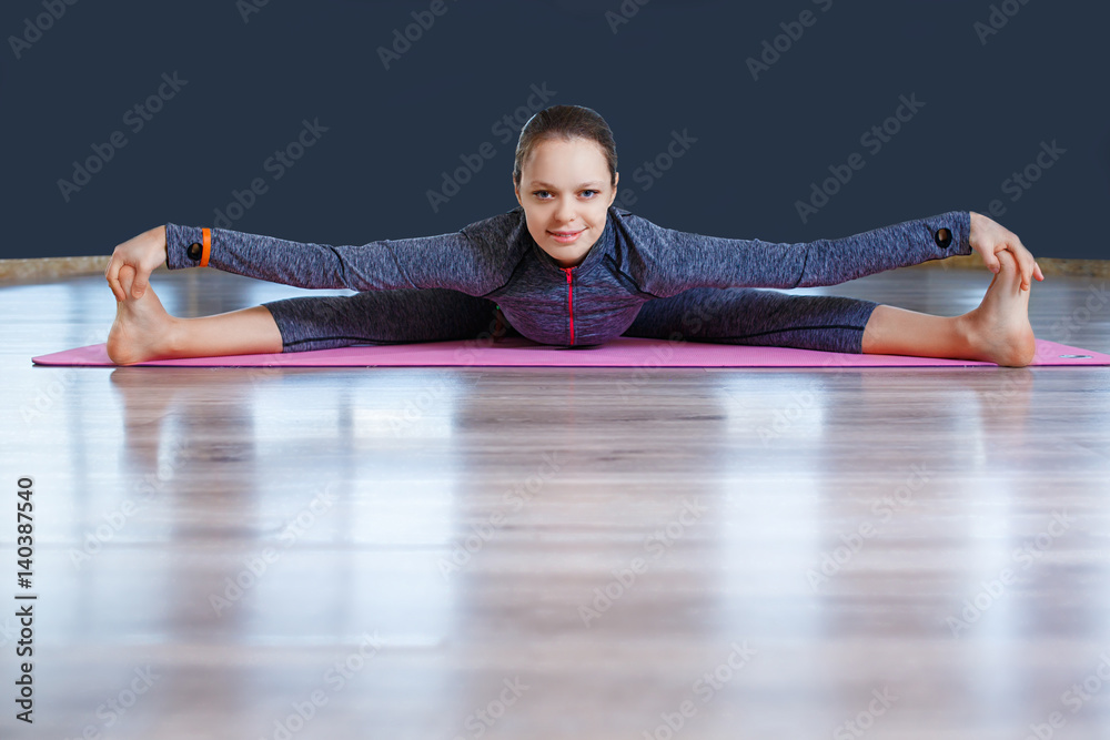 Beautiful young woman wearing blue sportswear set working out against blue wall, doing yoga or pilates exercise.