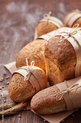 different bread on the wooden table, flour, paper bags, rope. Brown background.