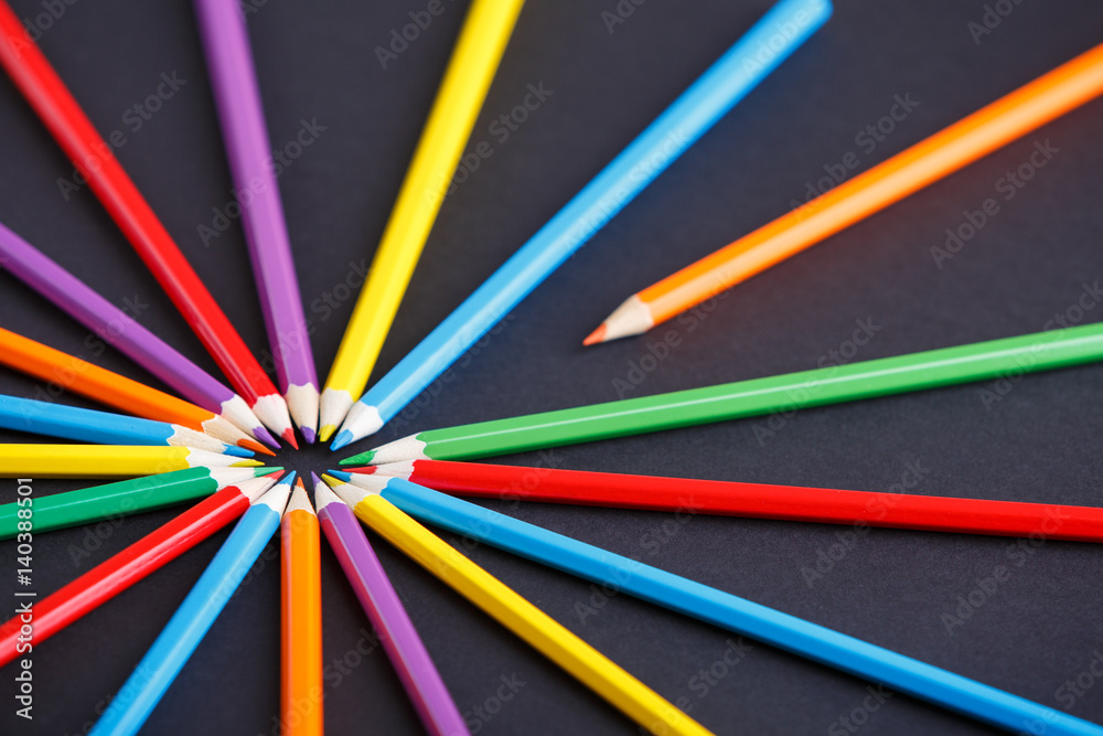 One orange pencil standing out from the circle of other colorful pencils on the dark background One orange pencil standing out from the circle of other colorful pencils on the dark background