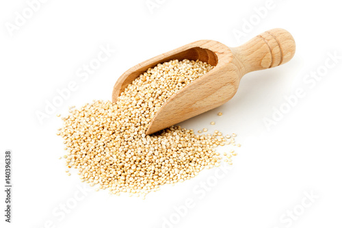 Raw, whole, unprocessed quinoa seed in wooden scoop on white