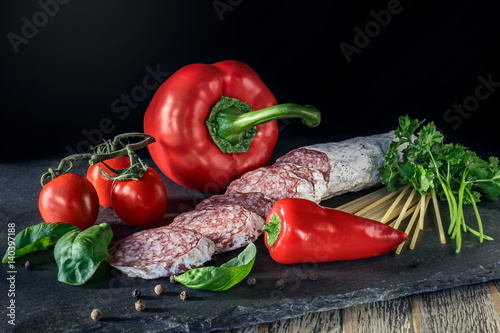 Salami with red paprika, tomatos  and pepper on the slate board