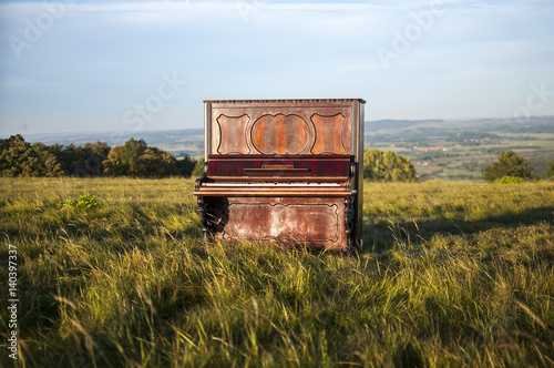 Old brown classical piano in the middle of the field outside and staying on the green grass