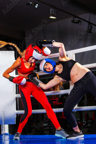 Two boxing women workout in fitness class. Sport exercise two female people .Boxer wearing red gloves to box and helmet in ring. Lower view angle.