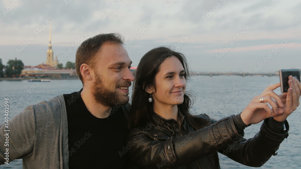 Beautiful young couple taking selfie on the background of river and the city. Peter and Paul Fortress, St. Petersburg 4K