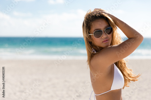 Sexy ethnic woman in white bikini and sunglasses on beach vacation