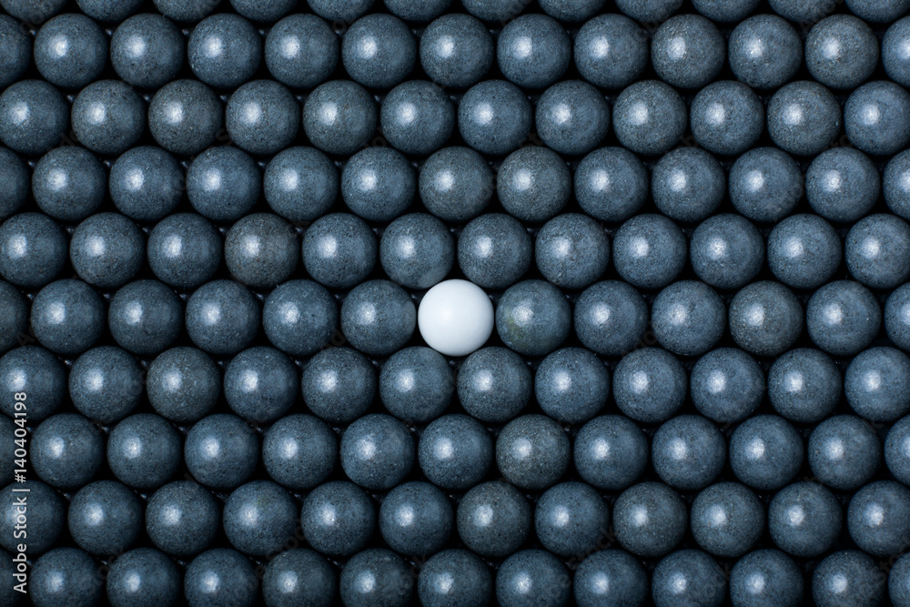 White airsoft ball is among many black balls. Background of 6mm bbs White airsoft ball is among many black balls. Background of 6mm bbs