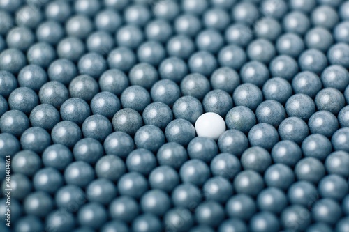 White airsoft ball is among many black balls. Background of 6mm bbs © Vasiliy