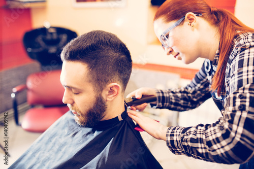 female hairdresser is cutting hair of bearded man client