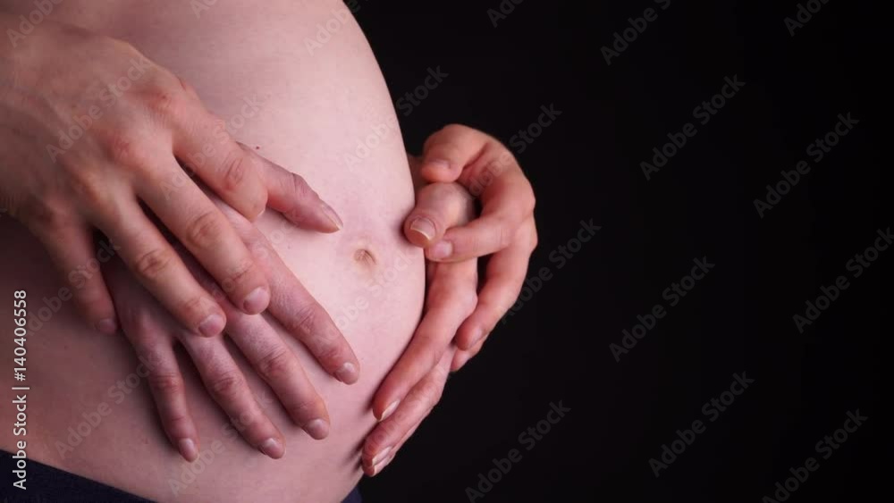 Couple with hands on naked belly of pregnant woman closeup on black background. Pregnancy, parenthood and baby anticipation concept. 4K ProRes HQ codec