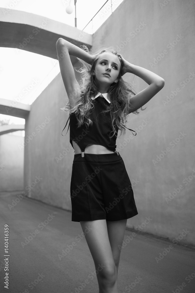 Schoolgirl in short holding her hair outside. Skinny girl in a tunnel.  Model posing outdoors. Cute teenager at the parking in the windy day. Black  and white fashion photography Stock Photo