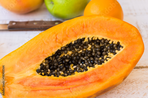 Very ripe juicy papaya cut in half on wood kitchen table with citrus fruits, apples, top view, closeup