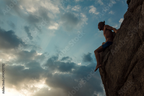 Man sittingon the edge. Side view of a man sitting and admiring the sunset on the edge of the rock.