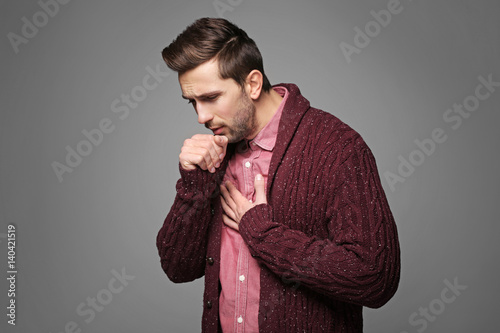Young man coughing on gray ...