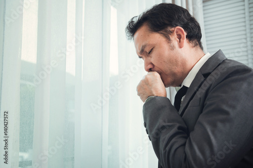Senior businessman in grey suit coughing. Illness, disease, allergy concepts.