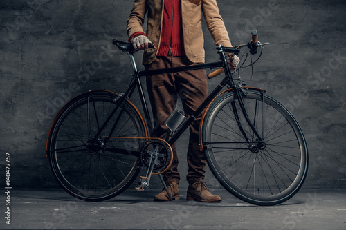 A man posing with single speed bicycle over grey background.