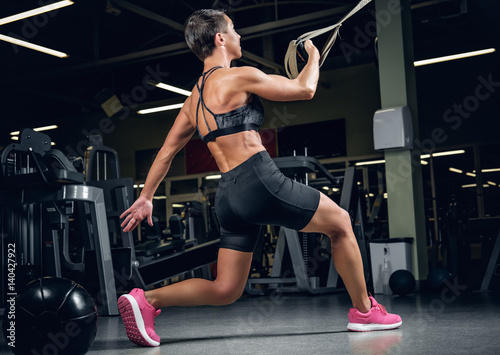 Female doing workouts with trx suspension strips in a gym club.