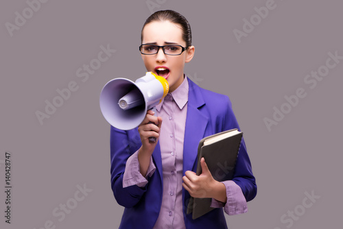 Young businesswoman with loudspeaker on gray background