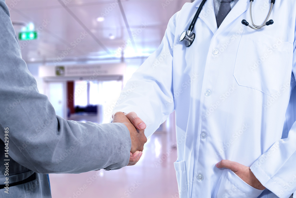 Doctor and Business man handshake with blurred hospital background