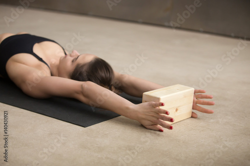 Photos Young attractive yogi woman practicing iyengar yoga using wooden block, lying on