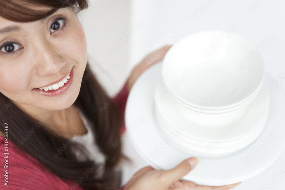 Portrait of young woman holding pile of plates, close up Portrait of young woman holding pile of plates, close up