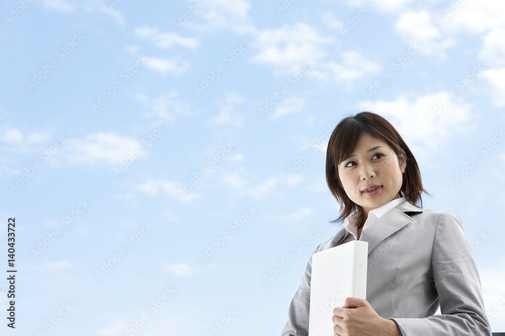 Young businesswoman looking away under sky, holding binder, copy space Young businesswoman looking away under sky, holding binder, copy space