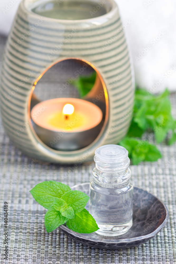 Peppermint essential oil in glass on gray mat with spa background, vertical Peppermint essential oil in glass on gray mat with spa background, vertical