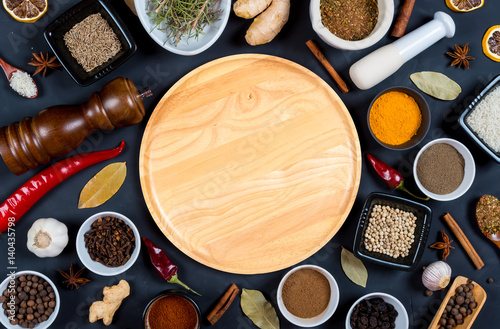 Indian spices, herbs and empty round cutting board on black background