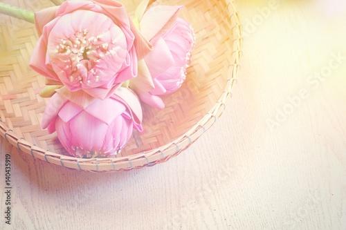 Pink lotus flower in basket and wooden background, spa concept. Blurry lilies and artificial light and copy space. Technical Writing Property artificial light.