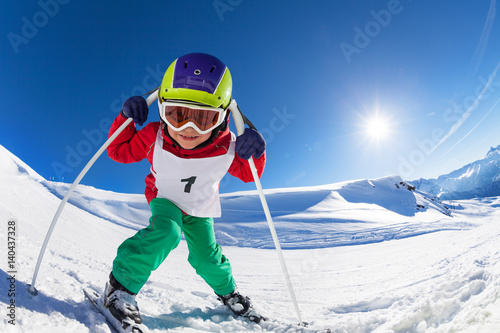 Cute little skier posing with poles at sunny day